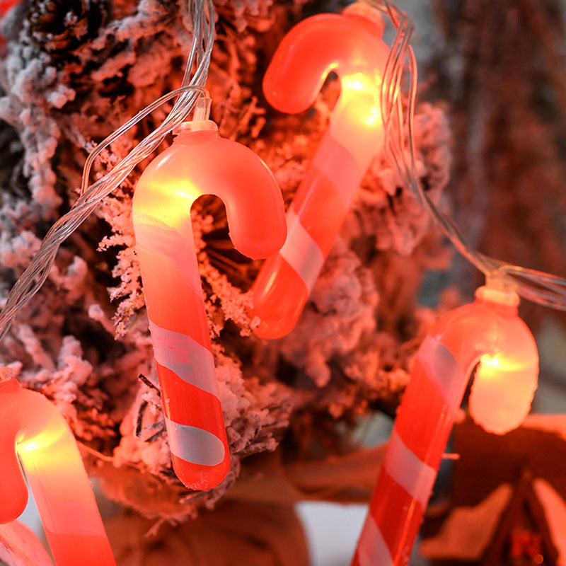 String lights shaped like candy canes and round bulbs against a blurred Christmas tree background.