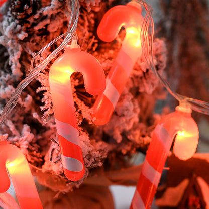String lights shaped like candy canes and round bulbs against a blurred Christmas tree background.