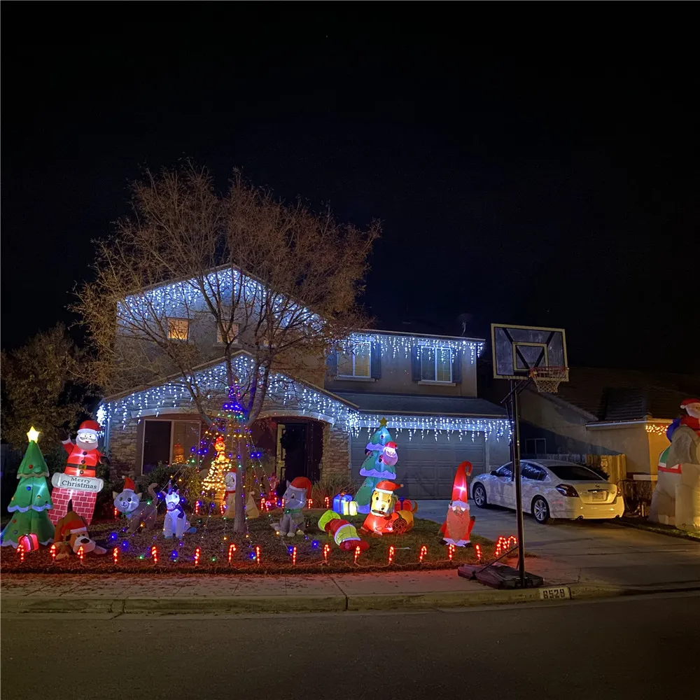 House decorated with Christmas lights and inflatable figures on a driveway at night.