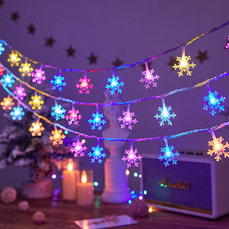 LED Snowflake Christmas String Lights on a festive background with candles and a Christmas tree.