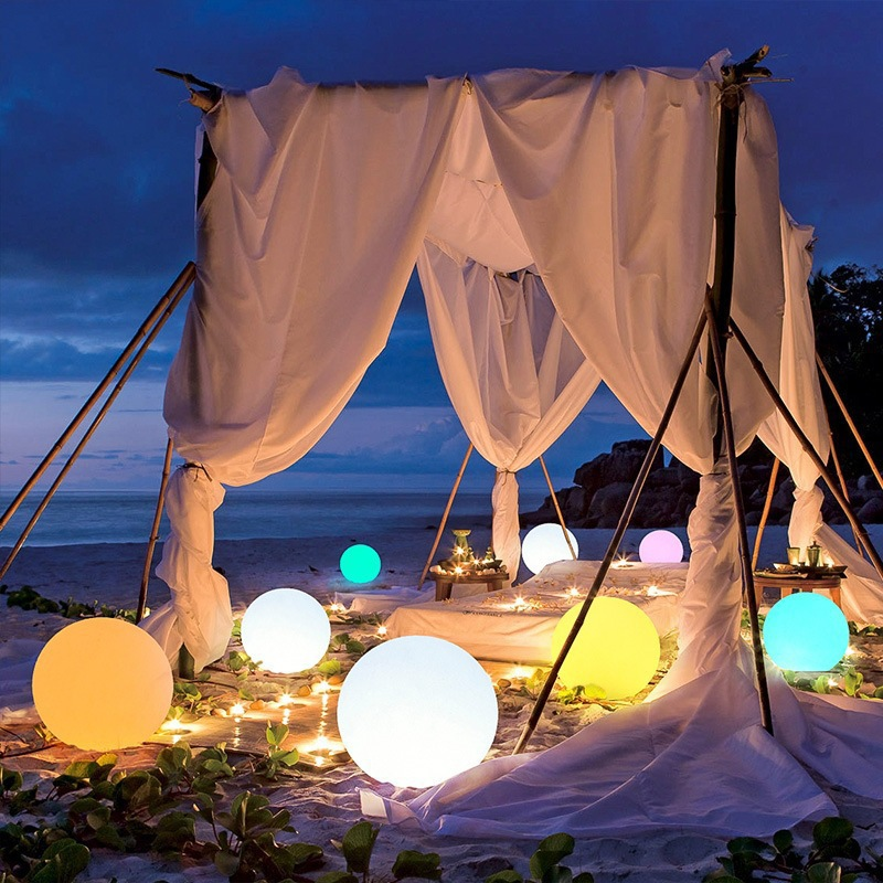 Decorative setup with white curtains, Modern LED Orb Lights Outdoor, and candles on a beach at night.