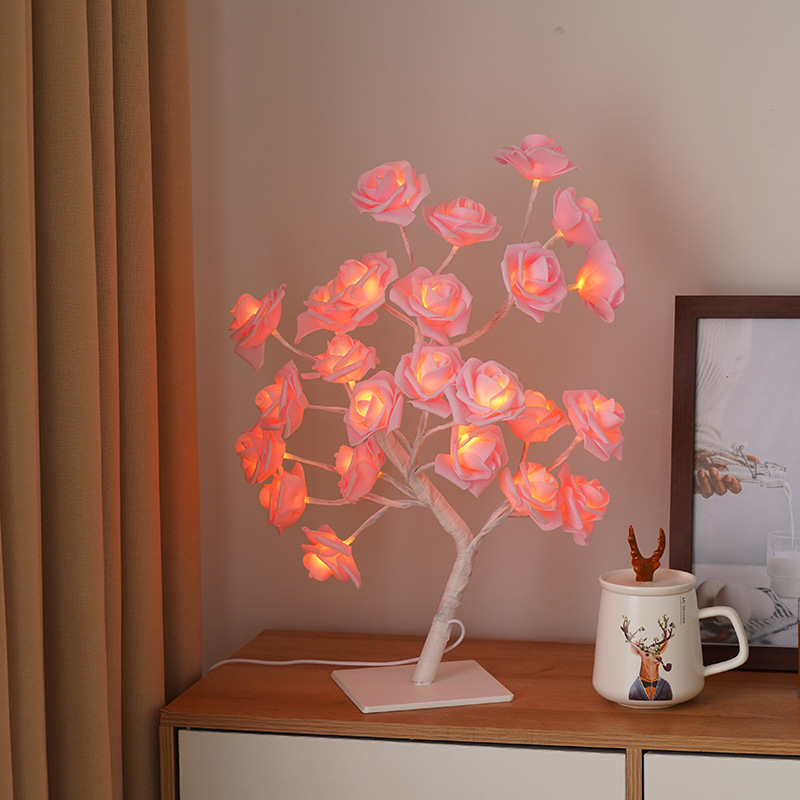 Decorative LED tree with pink flowers on a wooden surface next to a mug and photo frame.
