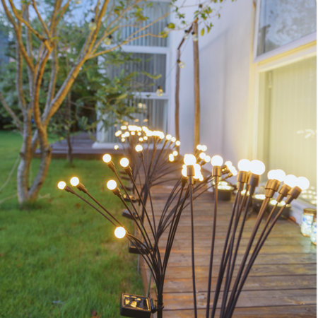 Solar Firework Garden Lights on a wooden deck with a garden and building in the background.