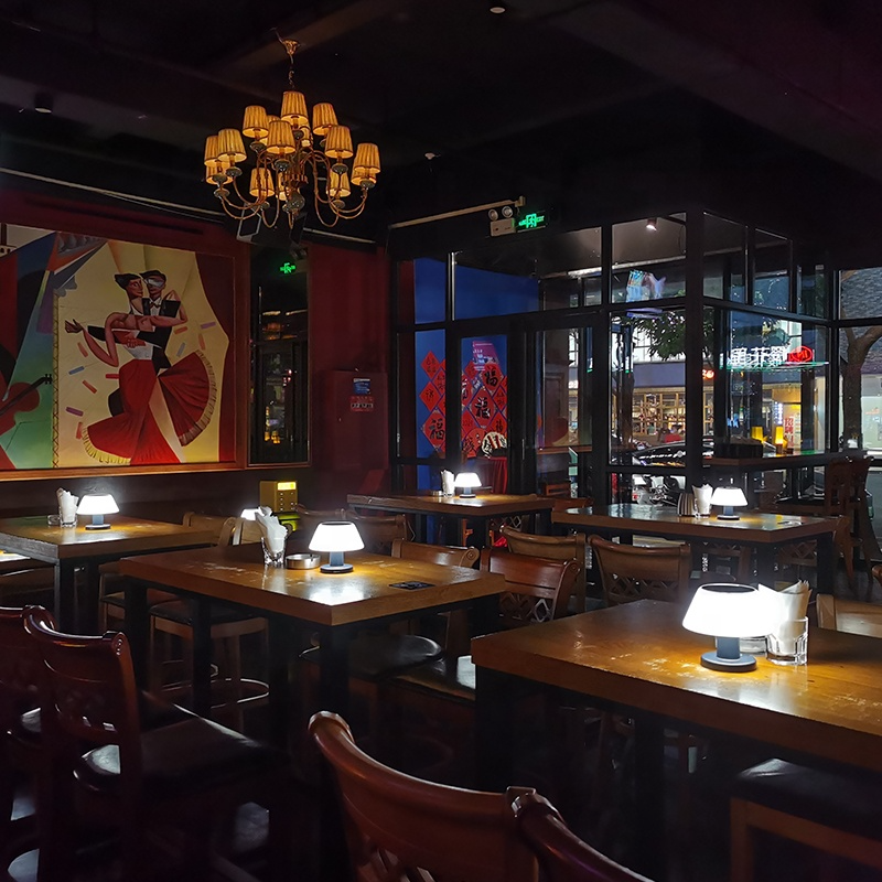 Solar Table Lamp Outdoor in Dark restaurant interior with tables, chairs, and decorative wall art.