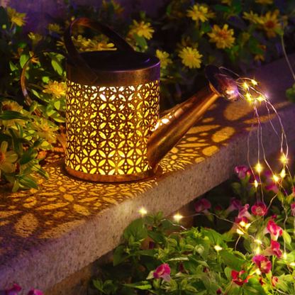 Solar Watering Can Garden Light casting a warm glow on a stone ledge with flowers in the background