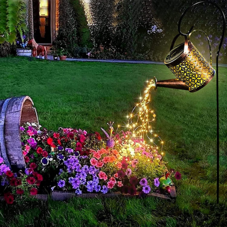 Solar Watering Can Garden Light like a watering can illuminating a garden bed with flowers.